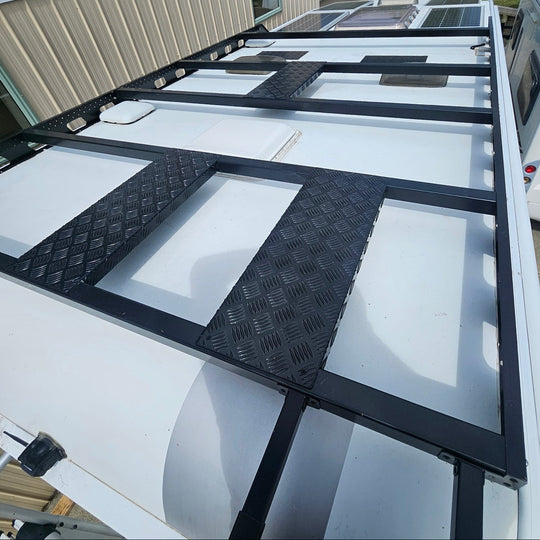 White RV with a black metal ladder and step platform, parked outdoors.